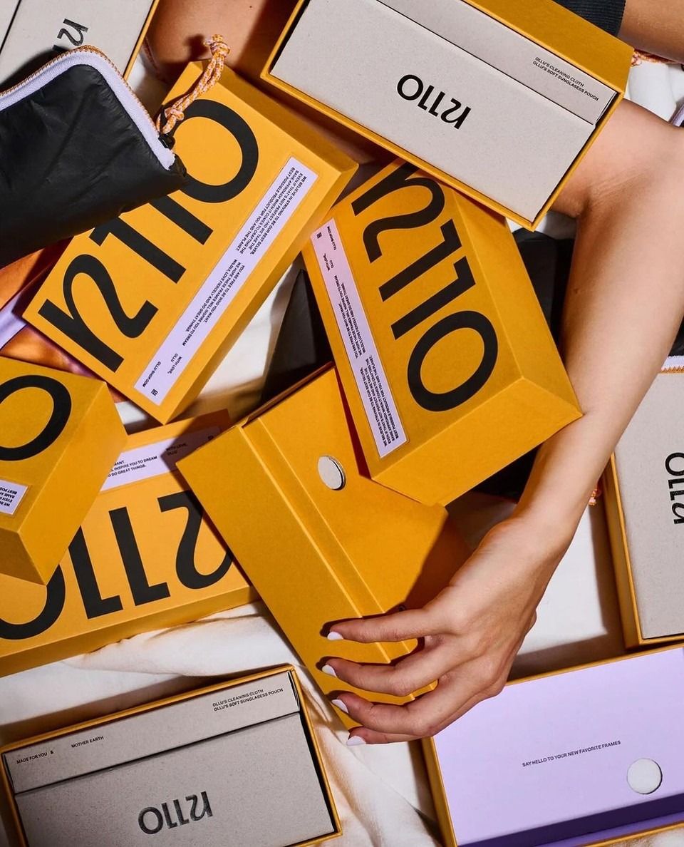Hands reaching through a pile of orange Ollo sunglasses boxes — grabby delight