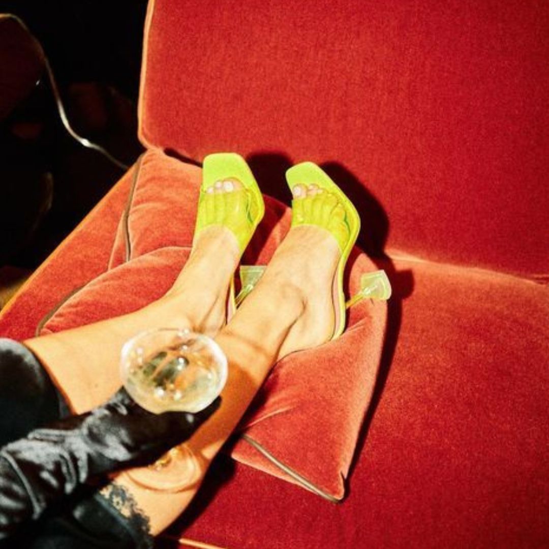 Neon heels on red velvet couch with wine glass — warm moody ambient