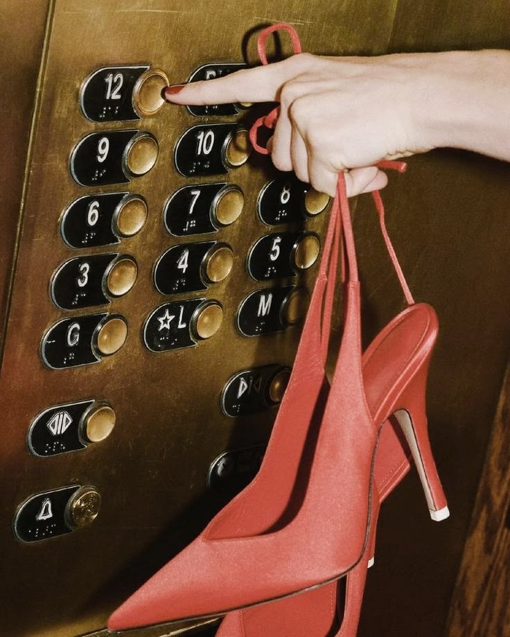 Red slingbacks dangling while pressing an elevator button