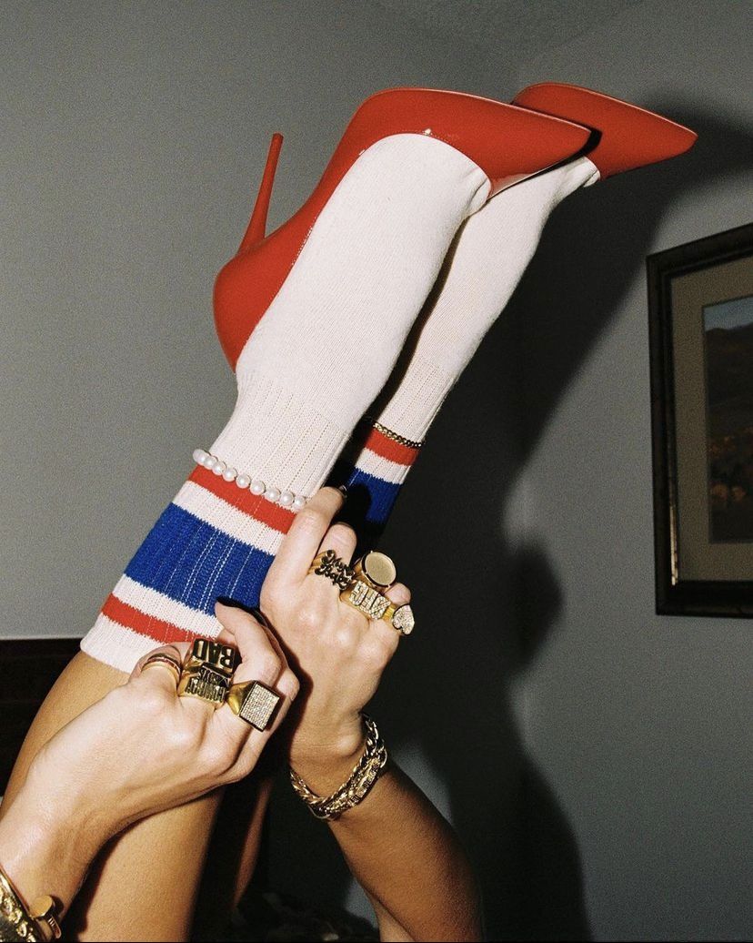 Hands covered in rings holding red pumps with striped socks