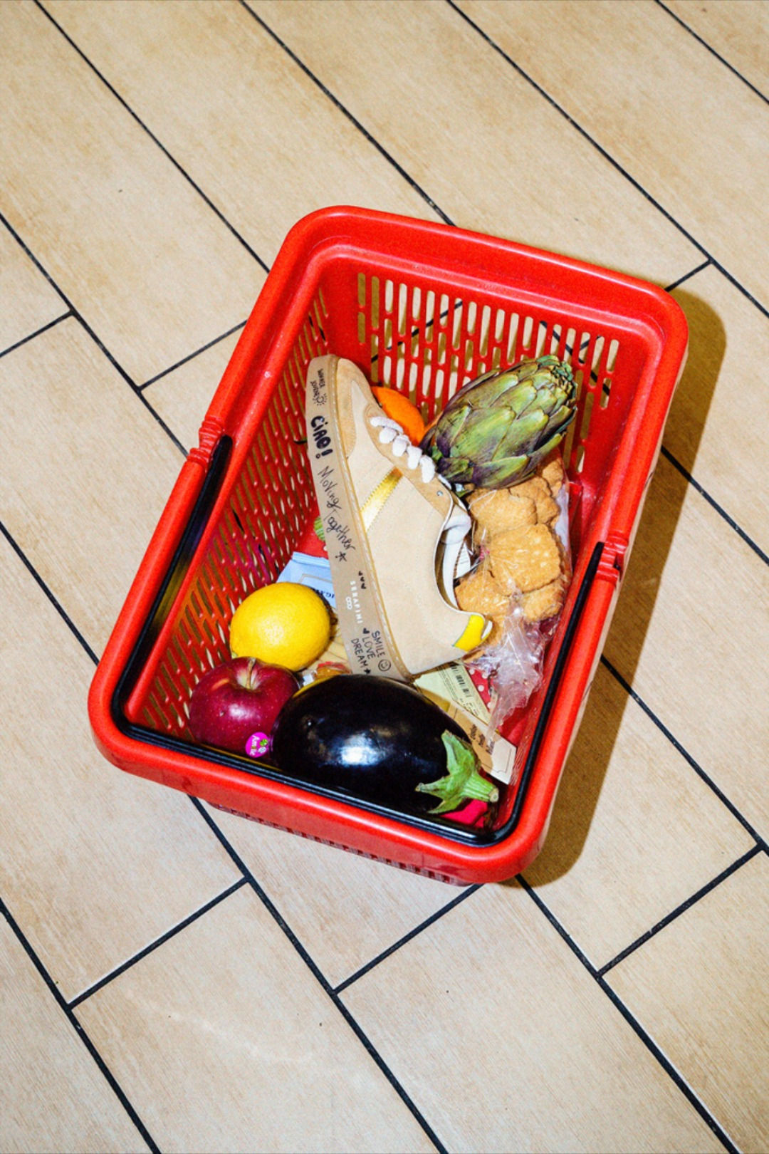 Red shopping basket overhead with shoe, artichoke, eggplant — surreal haul