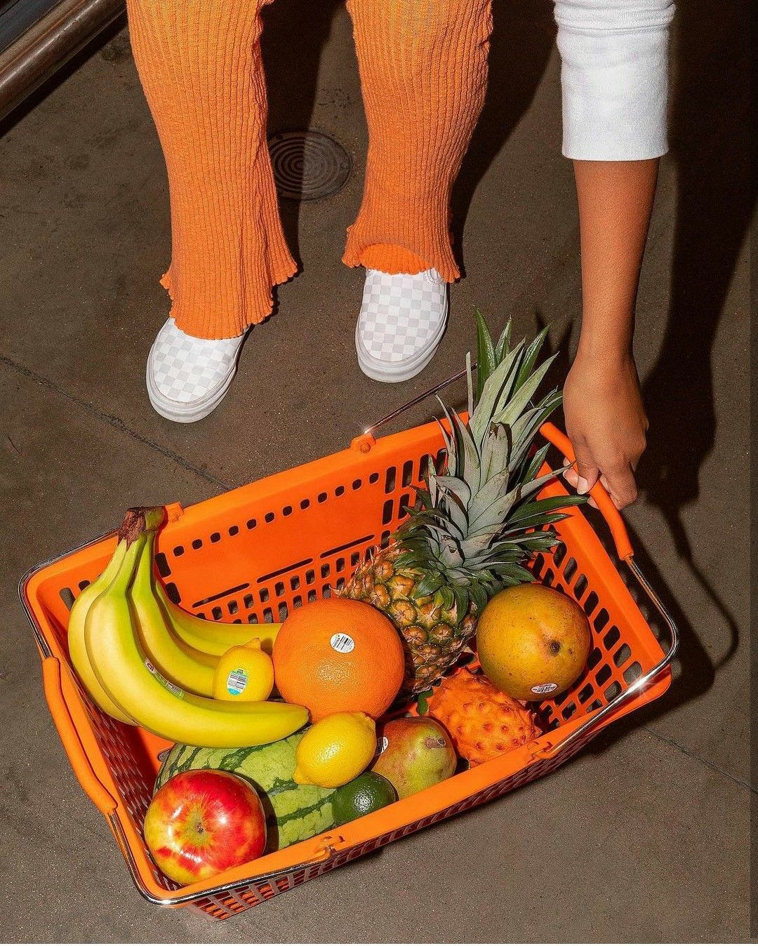 Orange grocery basket with tropical fruit — low-angle on tile